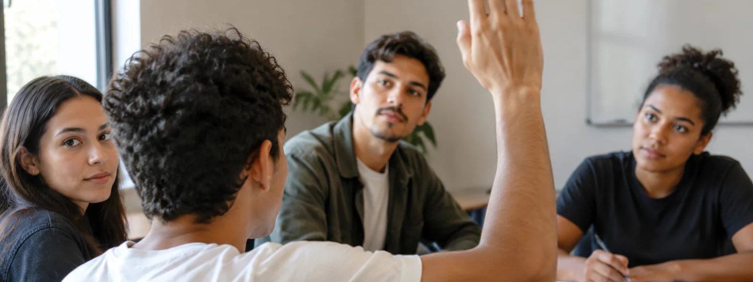 Participante com a mão erguida pedindo a vez, à mesa coberta de folhas escritas